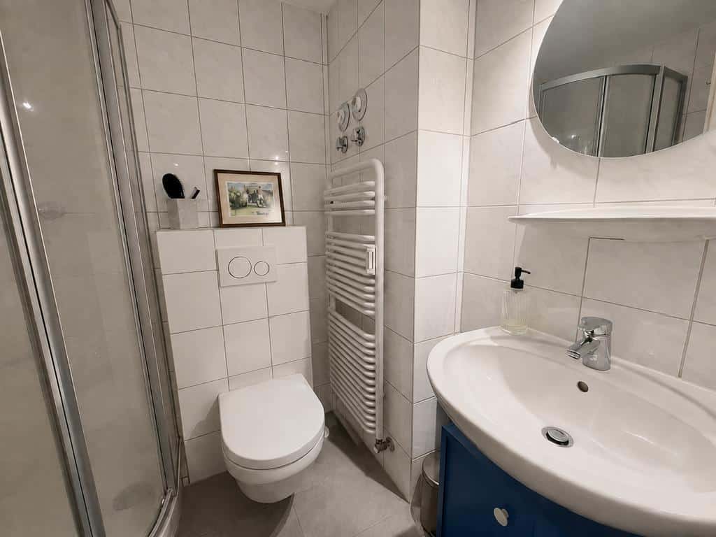 Gepflegtes, hell gefliestes Duschbad mit Handtuchheizkörper